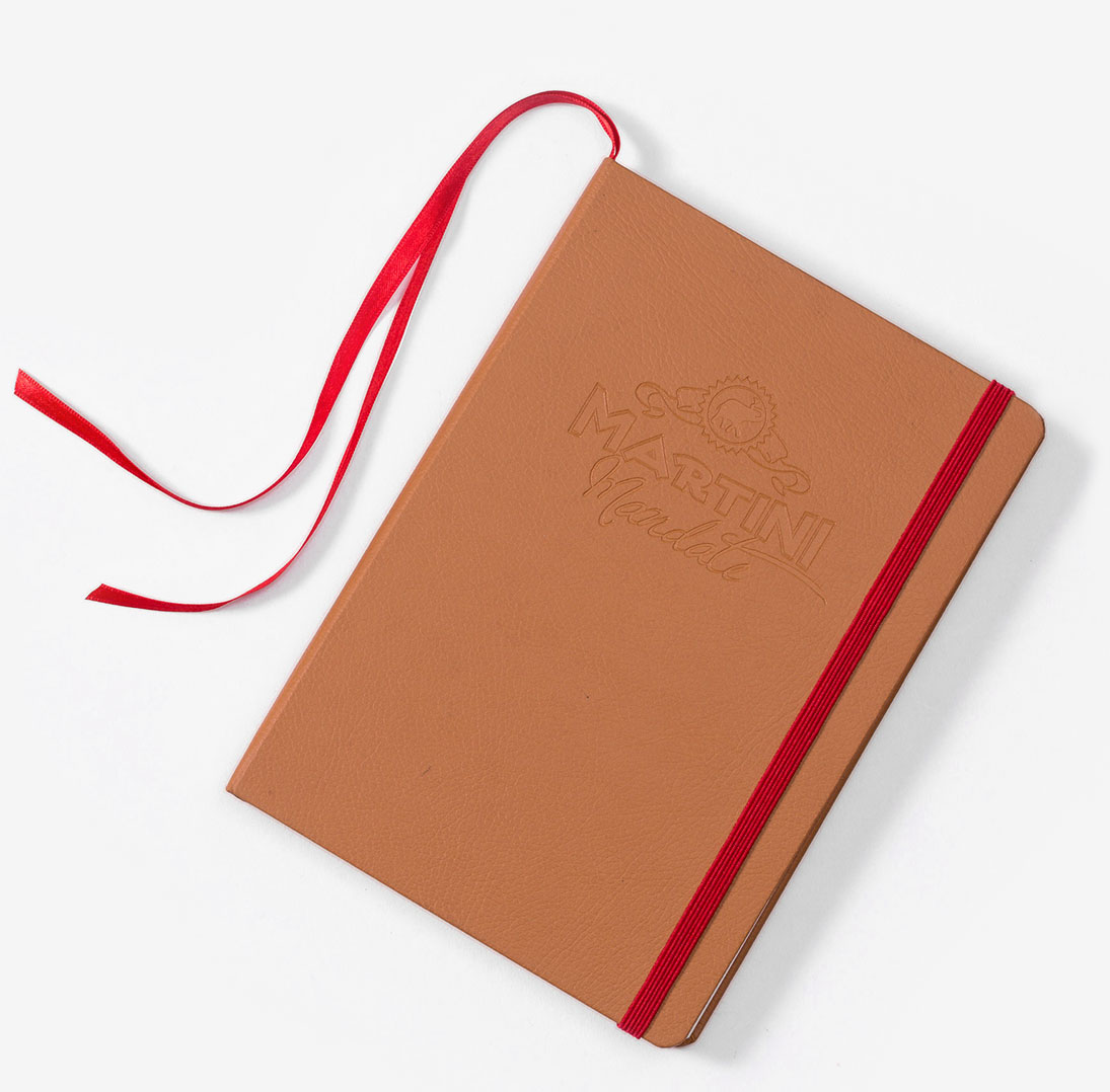 Tan faux leather notebook with debossed logo and red elatsic bands and ribbons