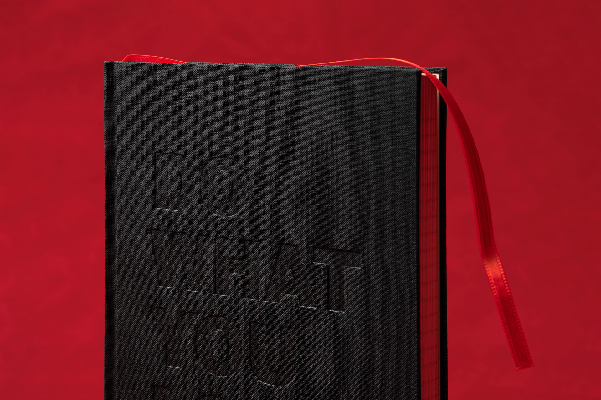 black clothbound notebook on red background with debossed letters